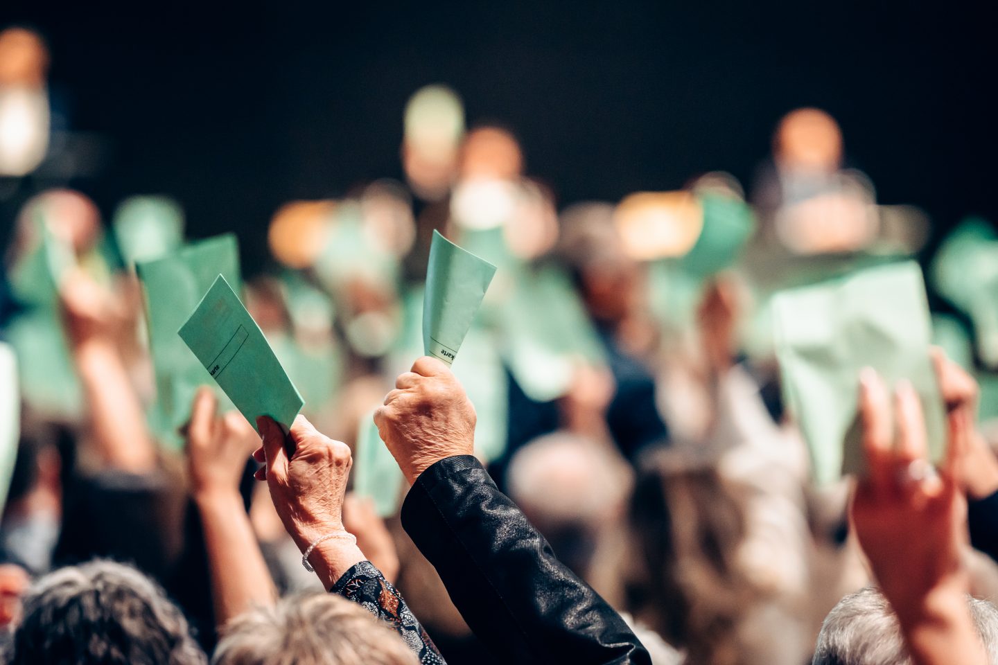 Die Genossenschafterinnen und Genossenschaften stimmen über die Fusion ab und halten den grünen Strimmrechtsausweis in die Luft. 