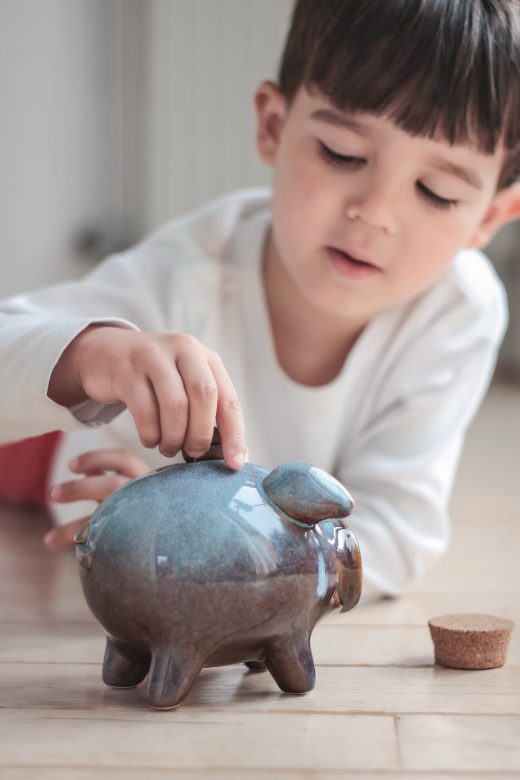 Kleiner Junge, der Geld in ein Sparschwein wirft