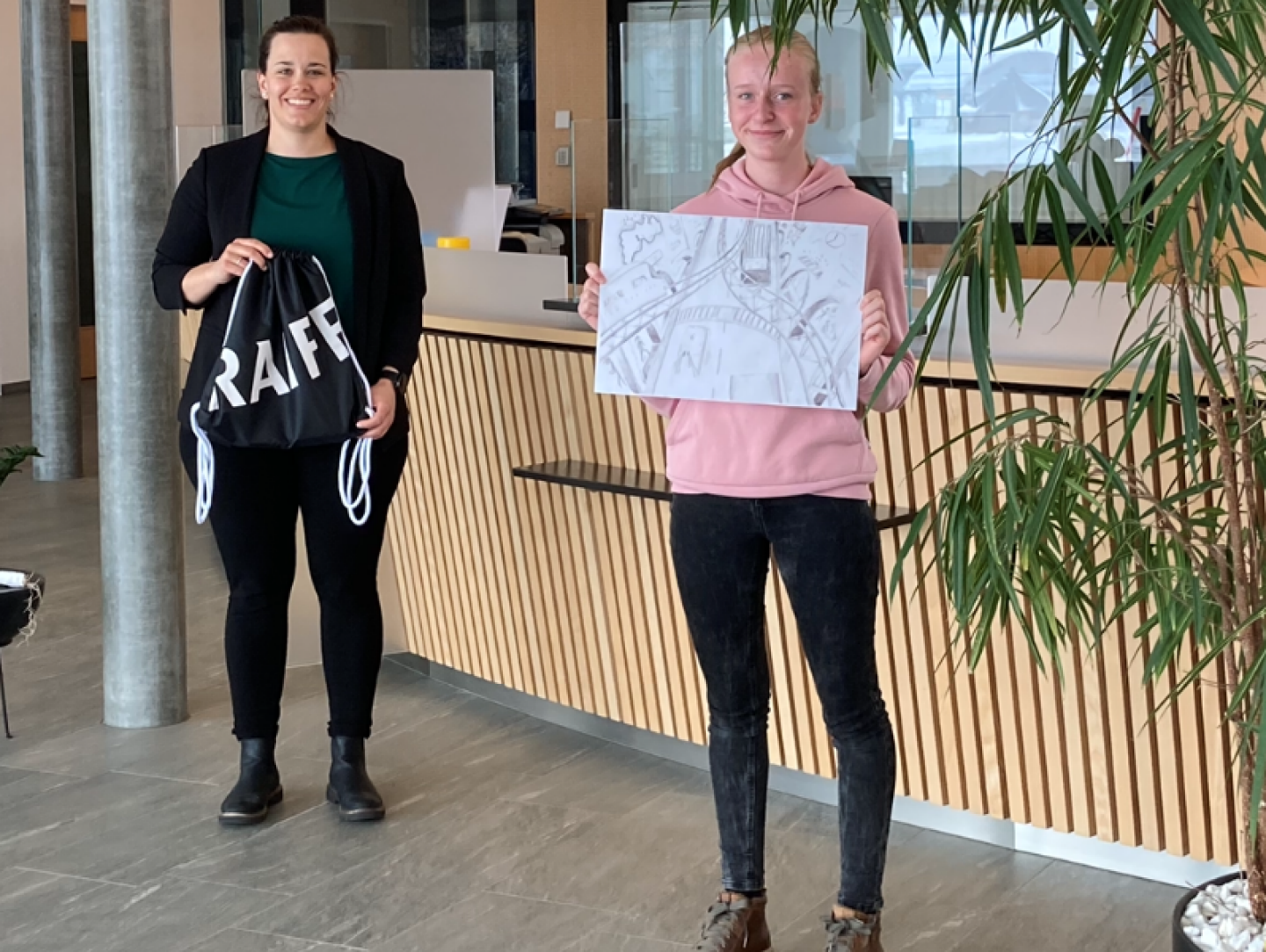 Alina Brunner hält stolz ihr Siegerbild in die Kamera. Kundenberaterin Laura Wyss übergibt ihr im Sportbag u.a. eine Raiffeisen-Musikbox.