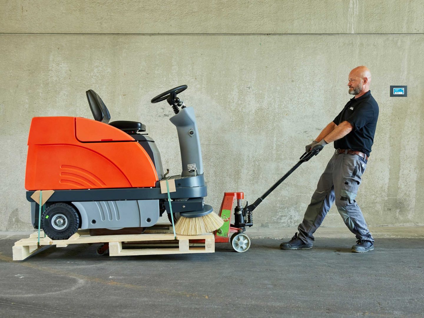 Ein Mitarbeiter zieht eine Reinigungsmaschine mit einem Handhubwagen.