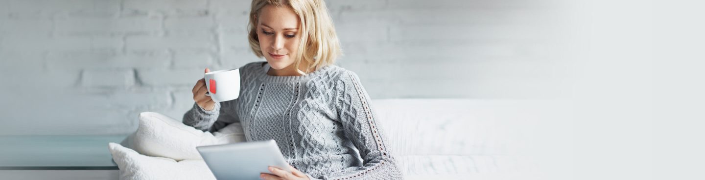 Frau trinkt Tee auf dem Sofa und studiert am Tablet die neuen Basisreglemente